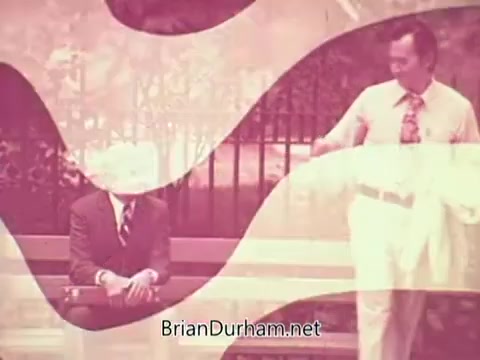 The still from the 'Job Service Ohio PSA' features two men in a park setting. One man, dressed in a suit, is seated on a bench, appearing contemplative. The other man, wearing a lighter-colored shirt and pants, stands nearby, possibly engaging in conversation. The image is stylized with a pink overlay and abstract shapes, creating a sense of warmth and approachability. The context suggests a focus on employment or job services.