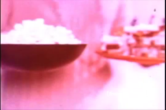 The still from 'Formica Floor Shine' showcases a visually striking scene, presented in vibrant, possibly altered colors typical of 16mm film. It features a bowl of what appears to be popcorn on the left and an assortment of cakes or pastries on a plate on the right. The background has a soft focus, enhancing the dreamy quality of the composition. The overall aesthetic evokes a nostalgic vibe, characteristic of mid-20th century film production.