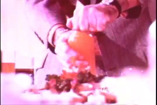 The still from 'Formica Floor Shine' showcases a close-up of a hand squeezing an orange, suggesting a domestic setting. The colors are vivid and slightly washed out, characteristic of 16mm film prints. In the background, there appears to be food items, hinting at a context related to cooking or food preparation. The overall mood feels vibrant yet nostalgic, reflecting mid-20th century aesthetic sensibilities.