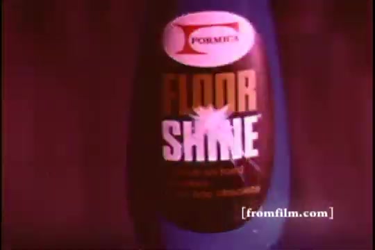 The still features a close-up of a bottle labeled 'FORMICA FLOOR SHINE.' The design is bold, with the words 'FLOOR SHINE' prominently displayed. The bottle is surrounded by a deep, vibrant background, likely enhancing the retro aesthetic typical of 16mm prints. The focus is on the product, likely emphasizing its shine-enhancing qualities.