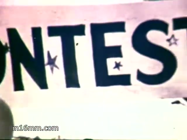 The still features a banner that reads 'CONTEST,' likely from a county fair setting. The voiceover highlights the longstanding tradition of awarding cooking prizes, particularly for dishes made with Mueller's egg noodles, emphasizing their special taste and popularity.