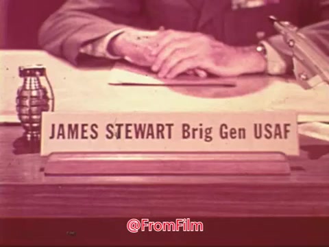 The still features a desk with a nameplate reading 'JAMES STEWART Brig Gen USAF.' In the foreground, a hand is visible, and a military-style grenade rests on the desk. The overall tone suggests a formal setting related to the Civil Air Patrol, emphasizing Stewart's role as a Brigadier General in the U.S. Air Force. The film's visual quality indicates it’s from the mid-20th century.