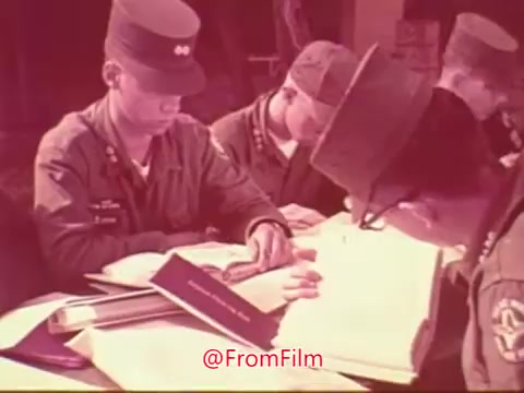 The still from the 'Civil Air Patrol PSA with Jimmy Stewart' features several young cadets in uniform, studying and focused on their work. They are seated around a table with books and materials spread out before them, indicating a learning or training session. The atmosphere is serious, highlighting the educational aspect of the Civil Air Patrol program. The image captures the dedication and commitment of the cadets.