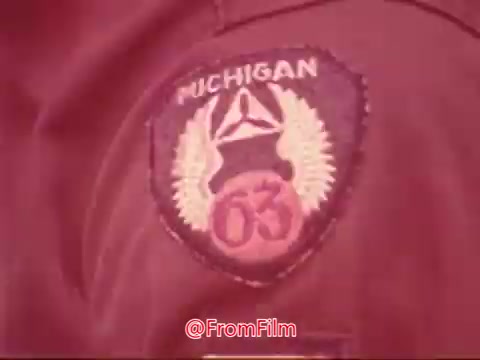 The 16mm still features a close-up of a Civil Air Patrol patch displaying the text 'MICHIGAN' and the number '63.' The patch is richly detailed, featuring an emblem with wings, indicating the affiliation to the Civil Air Patrol. The fabric appears to be part of a uniform, suggesting a connection to aviation or service activities.