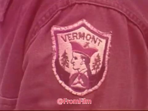 The still features a close-up of a patch displaying the word 'VERMONT' and an emblem, likely associated with the Civil Air Patrol. The design includes elements such as a figure, trees, and a distinctive shape, indicating a connection to the state and its organizations. The color and texture suggest it belongs to a uniform, emphasizing the theme of service and community involvement.