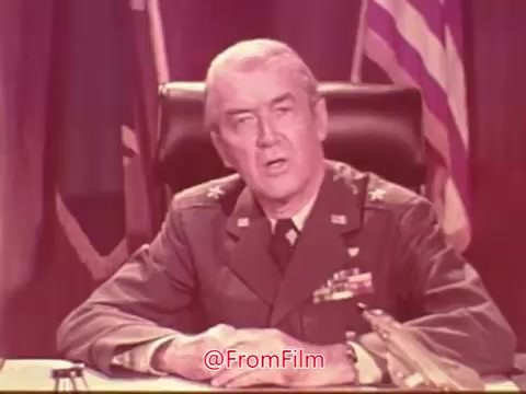 The still features James Stewart in a military uniform, seated at a desk with flags in the background. He appears to be addressing the audience earnestly, likely discussing the Civil Air Patrol and its importance. The setting conveys a serious tone, reflecting the themes of service and community involvement.