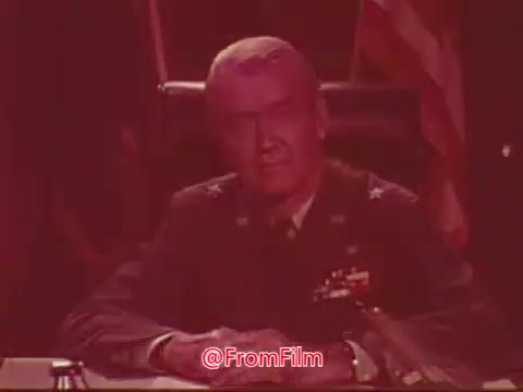 The still features a man in military attire, likely addressing the audience from a desk. He appears composed and serious, embodying a sense of authority. The setting includes an American flag in the background, emphasizing patriotism, which aligns with the promotional message of the Civil Air Patrol. The color tone gives a vintage feel typical of 16mm film from that era.