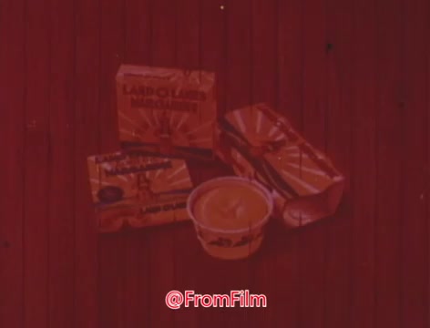 The still features packages of Land O'Lakes margarine prominently displayed against a wooden background. There are multiple butter sticks and a tub of margarine, all showcasing the brand's distinctive packaging. The overall color scheme appears warm, contributing to a nostalgic and inviting feel typical of vintage commercials.