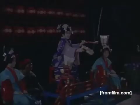 The 16mm still from the 'Pan American 'Far East Special' Trailer' (1963) captures a vibrant scene likely depicting traditional cultural elements. In the foreground, a performer dressed in a colorful kimono appears to be engaging in a traditional art form, possibly dance or theater. Surrounding her are other figures in period costumes, contributing to the rich visual tapestry of the moment. The backdrop suggests a theatrical setting, enhancing the performance's ceremonial or recreational aspect. This trailer serves as a promotional piece for a TV special sponsored by Pan American, emphasizing the exotic allure of the Far East during that era.