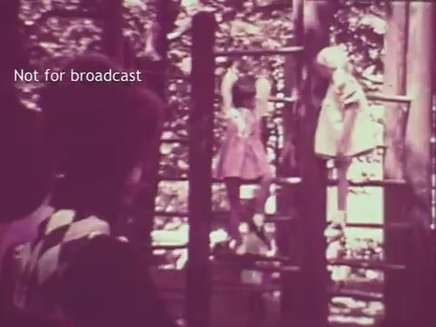 The still shows two children playing on a jungle gym in a bright, sunlit outdoor setting, likely a park or playground. One child is climbing while the other watches. The image has a vintage 16mm print aesthetic, featuring slightly muted colors characteristic of the 1960s. A watermark indicates it is not for broadcast.