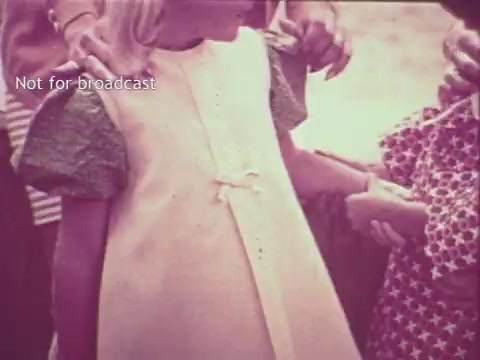 The still features a young girl wearing a light-colored dress, possibly showcasing the benefits of Pruf Spray Starch in maintaining a crisp look. Her dress has a bow detail, and she stands surrounded by adults and other children, indicating a relatable, family-oriented scene typical for 1960s commercials. The colors appear slightly muted, characteristic of a 16mm film print from that era.