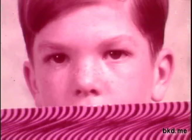 The still features a close-up of a young boy's face with a serious expression, predominantly in a reddish hue. His eyes are focused, and he has light freckles on his cheeks. The bottom portion of the image is decorated with a wavy patterned design, contrasting sharply with the simplicity of the child's face above. The overall aesthetic reflects the visual style of the 1970s, likely intended to draw attention to themes related to vision health.