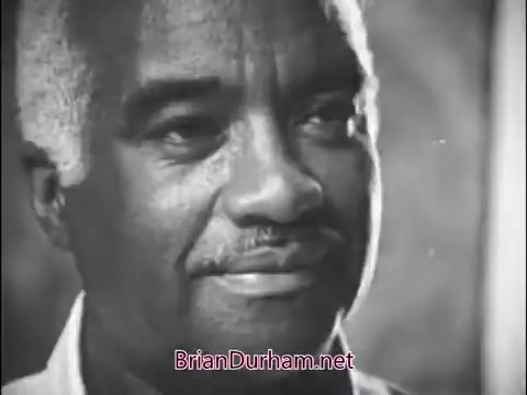 The still features a close-up of an older man with gray hair, wearing a white shirt. He has a warm expression, suggesting a thoughtful or content demeanor. The image likely captures a moment discussing community values or the impact of Girl Scouts in the 1960s. The overall tone is reflective and positive.