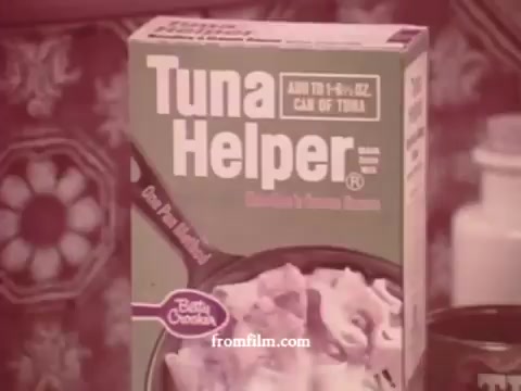 The still features a box of Tuna Helper, prominently displaying the brand name and a description, set against a vintage background typical of the 1970s. The packaging suggests ease of meal preparation, with an emphasis on its suitability for a can of tuna. The color palette and design reflect the period's aesthetic, capturing the era's advertising style.
