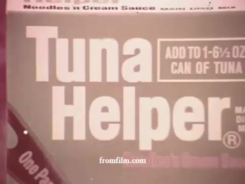 The still features a close-up of a 1970s Tuna Helper packaging. The label prominently displays the brand name 'Tuna Helper' in bold letters, emphasizing ease of preparation for a tuna dish. Key instructions are visible, indicating that the product is designed to be combined with a can of tuna, presenting it as a convenient meal option. The overall aesthetic reflects the design trends of the era, with a simple and straightforward presentation.