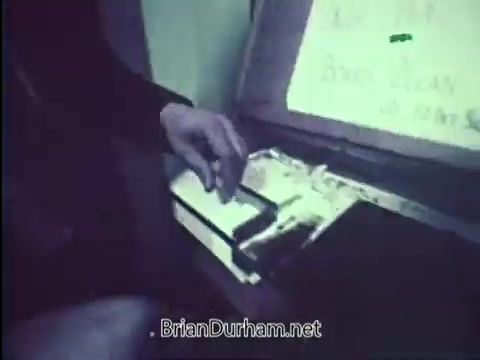 The still features a close-up of a hand reaching toward a vehicle's ignition or control panel, emphasizing the theme of car security. In the background, a sign likely underscores the importance of locking one's car, linking to the public service announcement's message about preventing vehicle theft. The visual seems to convey a sense of urgency and caution.