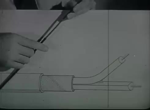 The still depicts a hand pointing at a diagram illustrating the construction of telephone drop wire. The diagram shows a cross-section of the cable, highlighting its different components, including the insulation and the conductors. This visual serves as an educational tool, demonstrating the technical aspects of connecting telephone lines from a utility pole to customer premises. The film likely aims to provide clear, step-by-step guidance on the installation process for telecommunications workers.