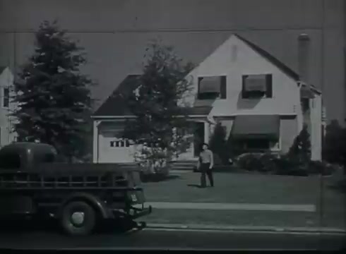 The still shows a suburban scene from the late 1940s to early 1950s, featuring a single-family house with a large lawn. A man stands in the yard, and a utility truck is parked near the curb. The house has awnings over the windows, and there are trees flanking the property. This setting likely represents a typical residential area where telephone drop wire installations are demonstrated, consistent with the educational purpose of the Bell System film.