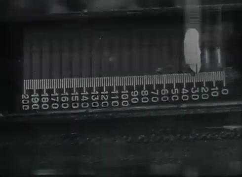 The still depicts a close-up of a measurement scale, likely used in a Central Office setting. The scale is marked with increments, possibly indicating wire lengths or measurements relevant to telephone installation. This part of the Bell System film emphasizes the precision required in the process of connecting telephone wires from utility poles to customers, showcasing the technical aspects of telecommunications infrastructure during the late 1940s to early 1950s.