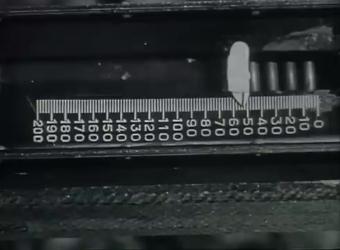 The still features a close-up of a measuring device, likely used in the installation or testing of telephone wires. The device displays a ruler-like scale numbered up to 200, indicating measurements for proper wire placement or management. This imagery reflects the technical processes involved in delivering telephone service from poles to customers as outlined in the Bell System film.