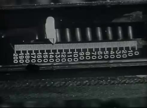 The still shows a close-up of a measuring device, likely used in the installation or maintenance of telephone wires. The scale is marked in increments, indicating measurements from 0 to 200. This type of footage is typical in training films from the late 1940s to early 1950s, illustrating the technical aspects of connecting telephone lines from poles to customer premises.