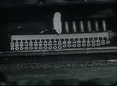 The still features a close-up of a measurement gauge, likely used in the context of installing or maintaining telephone wires. The gauge displays a scale marked in units (possibly inches or feet), showing a white marker pointing to a specific measurement. This detail emphasizes the precision needed in telephone wire installation, reflecting the technical aspects covered in the Bell System film on drop wire runs.