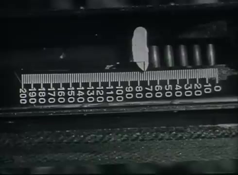 The still likely features a close-up of a measuring device or gauge, with a graduated scale ranging from 0 to 200. The context suggests it is part of a tutorial on the technical aspects of telephone wire installation, likely indicating measurements relevant to drop wire runs. The film is instructional, focusing on the methods and equipment used in the telephone infrastructure of the late 1940s to early 1950s.
