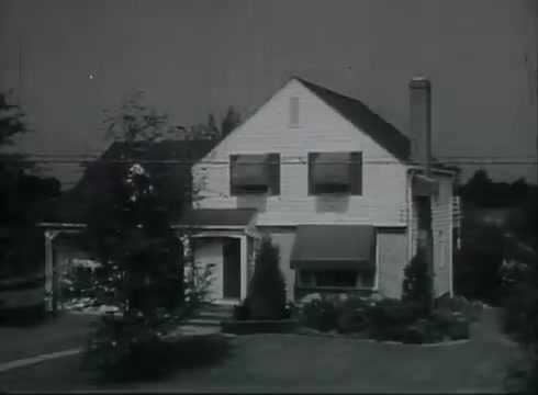 The still showcases a suburban house, likely from the late 1940s or early 1950s, with distinctive architectural features such as double-hung windows, a chimney, and neatly manicured landscaping. Power lines can be seen running overhead, illustrating the connection to the telephone service being discussed. The film likely serves to educate viewers on the process of delivering telephone wires from utility poles to residential homes. The black-and-white format adds a period-appropriate quality to the imagery, reflecting the era's style.