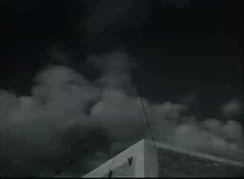 The still from 'Bell System Film - Drop Wire Runs Part 1 (b)' showcases a Central Office building under a cloudy sky. It likely represents the infrastructure involved in telephone service, highlighting the connection process from telephone poles to customer locations. The scene sets a technical and instructional tone, typical of educational films from the late 1940s and early 1950s, illustrating telecommunications methods of that era.