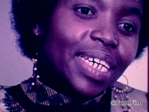 The still features a woman speaking passionately, likely during a segment of the World Day of Prayer event on March 7, 1975, organized by Church Women United. She wears a patterned garment and earrings, suggesting a cultural expression. The focus appears to be on her message, conveying the spirit of community and prayer emphasized during the event.