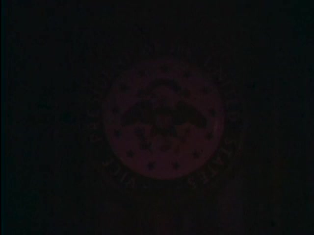 The still features the Great Seal of the Vice President of the United States, prominently displayed. The image appears dim, emphasizing the seal's design, which includes an eagle and a circle of stars. This context relates to a 1967 public service announcement featuring Vice President Hubert Humphrey, promoting the message of staying in school. The overall atmosphere is serious, underlining the significance of the message being conveyed.