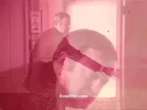 The still appears to be from a vintage 16mm commercial, likely from the 1970s, depicting a man entering a bathroom. The colors are notably tinted in red, creating an impressionistic effect. His expression suggests surprise or anticipation, potentially in response to a fresh scent or cleaning experience linked to the Airwick Bathroom tablet. The imagery evokes a sense of nostalgia, characteristic of advertising from that era, and highlights the influence of scent and cleanliness in bathroom products. The background may hint at typical retro decor.