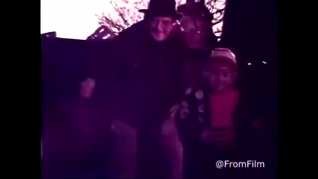 The still from the 'C&P Telephone commercial - 1970's - Bell Telephone' features a cheerful scene with an older man and a child, likely enjoying a festive moment together. The imagery is warm and nostalgic, typical of advertisements from that era, emphasizing connection and family. The commercial promotes the tagline 'The next best thing to being there,' aligning with C&P Telephone's messaging to highlight communication. The print showcases a faded, vintage aesthetic characteristic of 16mm film, further enhancing the sense of nostalgia.