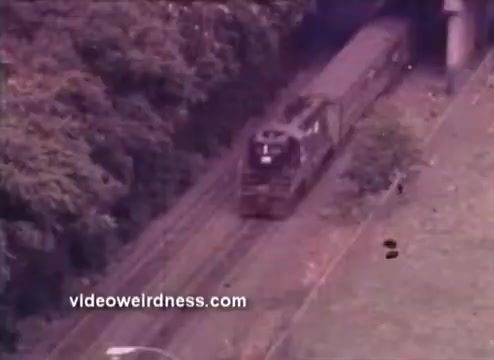 The still features a train traveling along tracks, surrounded by greenery. The image has a vintage quality characteristic of 1970s film, possibly emphasizing themes of environmental awareness. The context suggests it may be part of a public service announcement by the EPA, highlighting transportation and its impact on the environment.