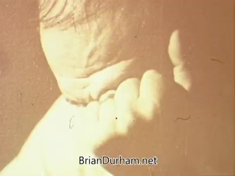 The still captures a close-up of a man's face, displaying a pained or contemplative expression as he rests his chin on his hand. The lighting gives the image a warm, sepia tone, adding to the somber atmosphere. This visual likely supports a message about the struggles associated with alcoholism, reflecting themes of distress and introspection common in public service announcements from that era.