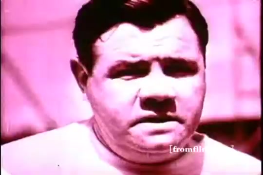 The still features a close-up of Babe Ruth, with a serious expression. The image has a pink tint typical of 16mm prints from the 1970s, portraying a nostalgic feel. Ruth's attire appears simple, likely reflecting a casual moment during the promotion of Kellogg's Corn Flakes. The background is blurred, focusing the viewer's attention on his face.