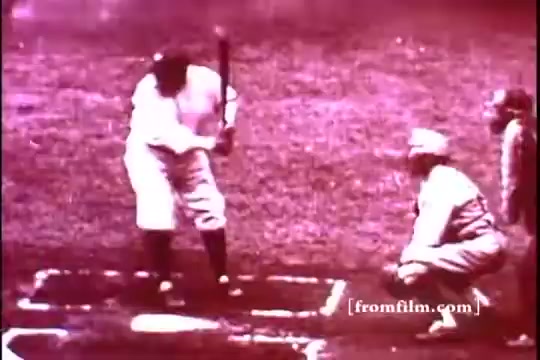 The still features Babe Ruth at bat in a vintage baseball scene. He's poised to hit, with a bat in hand, while a catcher crouches behind home plate. The image has a sepia tone typical of 1970s film prints, capturing the nostalgic essence of America's pastime. The background suggests a baseball field, evoking a sense of history and classic American sports culture.