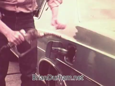 The still shows a close-up of a person filling a car's gas tank with a fuel pump nozzle. The individual appears to be dressed in casual attire, and the car is likely from the 1970s era, reflecting the time period of the PSA. The context suggests a focus on job-related themes or economic activities in Ohio during that decade.