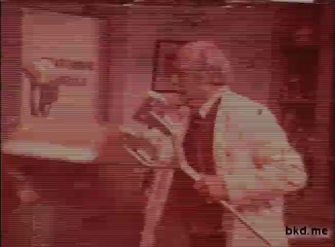 The still shows a scene from a 1960s-1970s Spic and Span TV commercial. The image features a man dressed in a white coat, likely portraying a comedic or exaggerated character. He carries a cleaning tool, possibly a mop or broom, suggesting an emphasis on cleanliness or a humorous take on cleaning tasks. The overall aesthetic is indicative of television production from that era, with a slightly faded quality typical of 16mm prints.