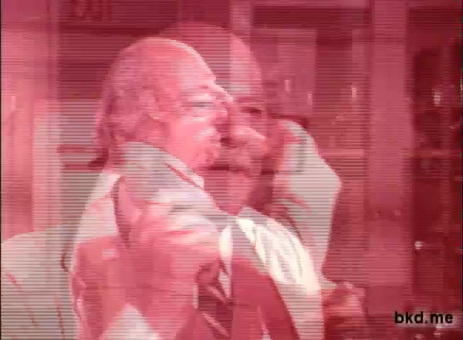 The still features a blurry and stylized image from a 16mm print of a 1960s-1970s Spic and Span TV commercial. It captures a male figure, possibly a spokesperson, in a dynamic pose, suggesting enthusiasm or a demonstration. The color palette has a reddish tint, contributing to an old film aesthetic, while visual distortions hint at the age and wear of the film used. The background appears somewhat cluttered, typical of commercial settings from that era.