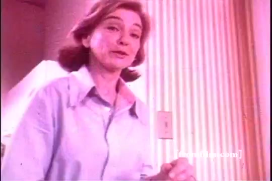 The still features a woman with shoulder-length hair, dressed in a light blue shirt. She appears to be speaking directly to the viewer, likely promoting Downy Fabric Softener. The background includes striped wallpaper, contributing to a vintage domestic setting typical of 1970s commercials. The overall color tone is warm and soft, characteristic of that era's advertising style.