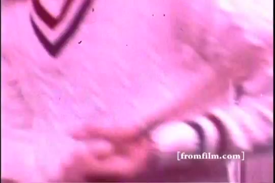 The still from the 1970s Downy Fabric Softener commercial features a close-up of a person wearing a light-colored sweater with a distinctive V-neck and stripes. The focus is on their hands, possibly demonstrating softness or handling freshly laundered fabric. The overall color tone has a nostalgic, slightly faded quality typical of vintage film imagery.