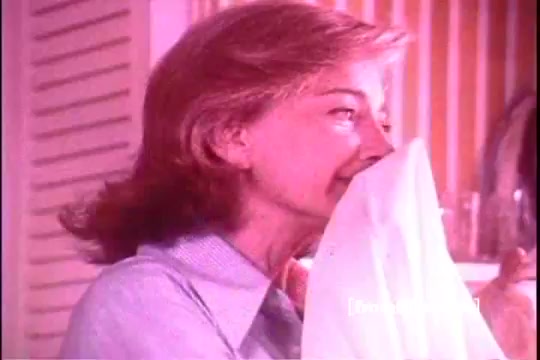 The still features a woman with a warm expression, joyfully smelling a freshly laundered white fabric, likely a towel or sheet. She is dressed in a light blue blouse, and the background suggests a cozy, domestic setting typical of 1970s advertisements. The overall tone is bright and cheerful, reflecting the positive emotions associated with using Downy Fabric Softener.