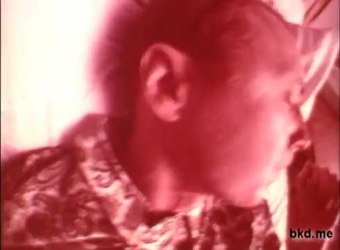 The still features a close-up of a man in a patterned shirt, appearing to be in a relaxed or reclining position. The image has a reddish tint, typical of older film prints, suggesting it may have been processed or exposed in a specific way. The overall atmosphere is likely intended to convey a comforting or therapeutic feeling associated with the product being advertised.