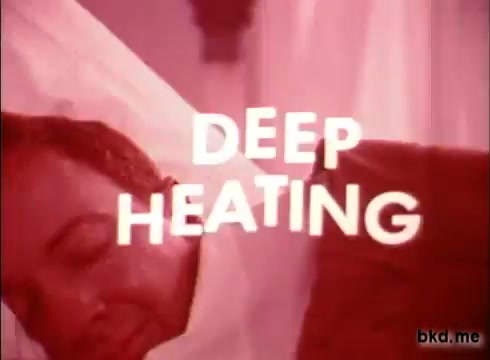 The still features a man resting or sleeping, with the phrase 'DEEP HEATING' prominently displayed in bold, stylized text. The overall color tone is warm, likely with pink or red hues, which enhances the relaxed atmosphere. The image suggests a focus on comfort and relief, typical of a product commercial from the 1970s.