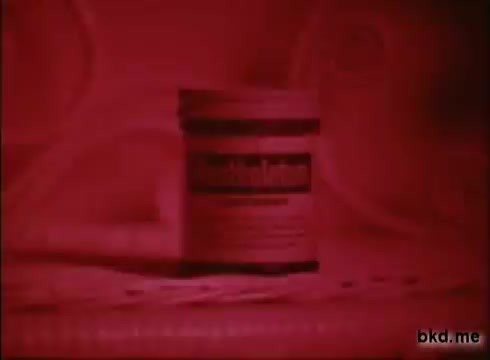 The still features a jar of Mentholatum prominently displayed against a red-tinted background. The focus is on the product, with the label clearly visible, emphasizing its branding. The composition creates a retro aesthetic typical of 1970s commercials.