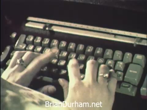 The still captures a close-up of hands typing on a typewriter, illustrating the focus and diligence of secretaries at Hemisfair '68 in San Antonio. The context highlights their dual role of managing office correspondence while participating in the festivities of Secretaries' Week. Their environment suggests a blend of work and leisure, with nearby attractions like the US pavilion providing a backdrop to their responsibilities.