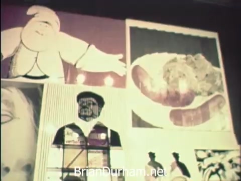 The still from 'News Item - Secretaries at Hemisfair '68' depicts a colorful arrangement of artworks or posters, showcasing various illustrations. The focus seems to be on a whimsical character, possibly a chef or a vendor, alongside images of food items, emphasizing the lively atmosphere of the event. This visual captures the blend of work and leisure experienced by secretaries during Secretaries' Week, highlighting a moment of creativity and enjoyment amidst their professional responsibilities at the World's Fair.