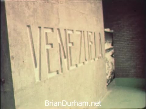 The still from 'News Item - Secretaries at Hemisfair '68' features a concrete structure prominently displaying the word 'VENEZUELA.' This scene encapsulates the atmosphere of the 1968 Hemisfair in San Antonio, highlighting the international pavilion dedicated to Venezuela. The context reveals that while secretarial staff enjoy intriguing moments during Secretaries' Week, they remain committed to their office responsibilities amidst the world's fair activities.