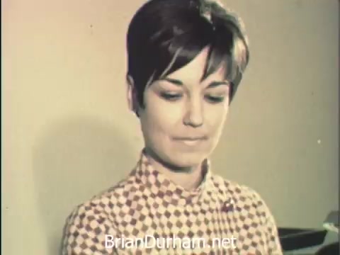 The still from 'News Item - Secretaries at Hemisfair '68' captures a woman with short hair, focused on her work, likely during Secretaries' Week. Dressed in a patterned blouse, she embodies the balance between administrative duties and the opportunities for exploration and social interaction amidst the backdrop of the Hemisfair event in San Antonio. The atmosphere reflects a blend of dedication to office responsibilities and the vibrancy of the world's fair.